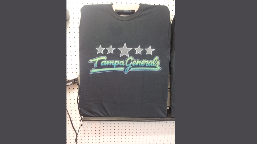 A black t-shirt with the words "Tampa Generals" and star designs airbrushed in vibrant colors. The image demonstrates the visual appeal of airbrushed designs on dark fabrics, which are not ideal for events due to the extensive priming and drying time required.